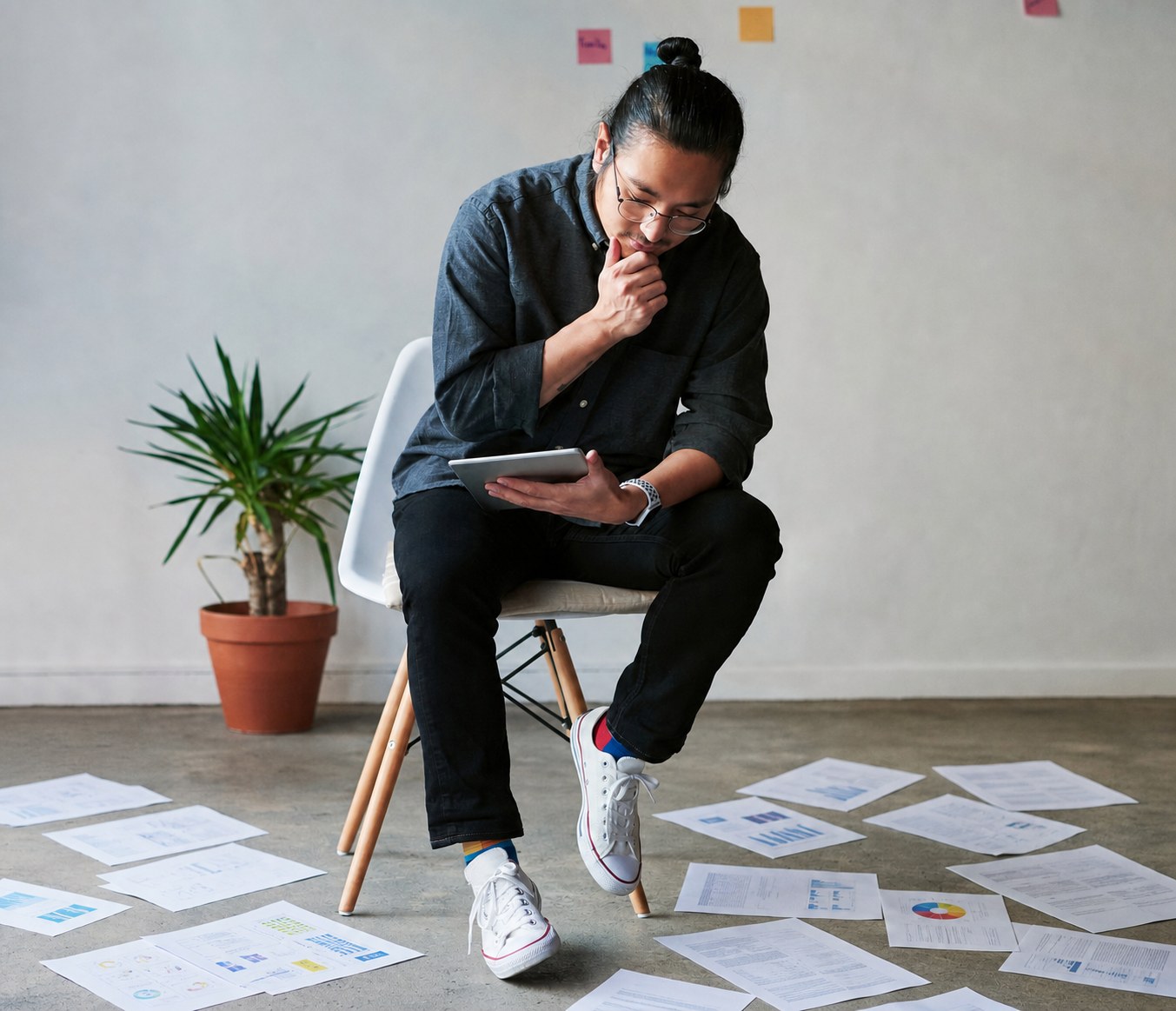 An analyst reviewing a tablet with research papers spread across the floor